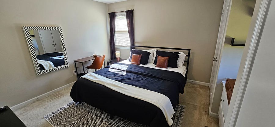 Primary Suite with a king-sized bed, cozy reading nook, flat-screen TV, desk, mirror, dresser, two closets, room-darkening/blackout curtains, and a private bathroom.