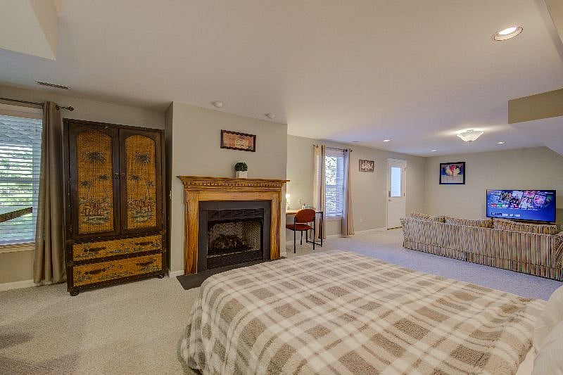 View of queen bed, with wardrobe, fireplace, reading desk, couch and smart TV.