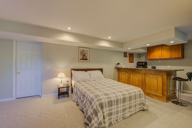 Queen bed with view of kitchen and bar stool.