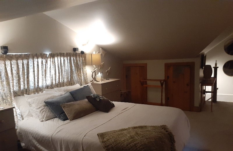 View from bathroom toward stairs. Bedroom with vaulted ceilings which are low in side areas. Hanging closets and chest of drawers. Window overlooking patio.
