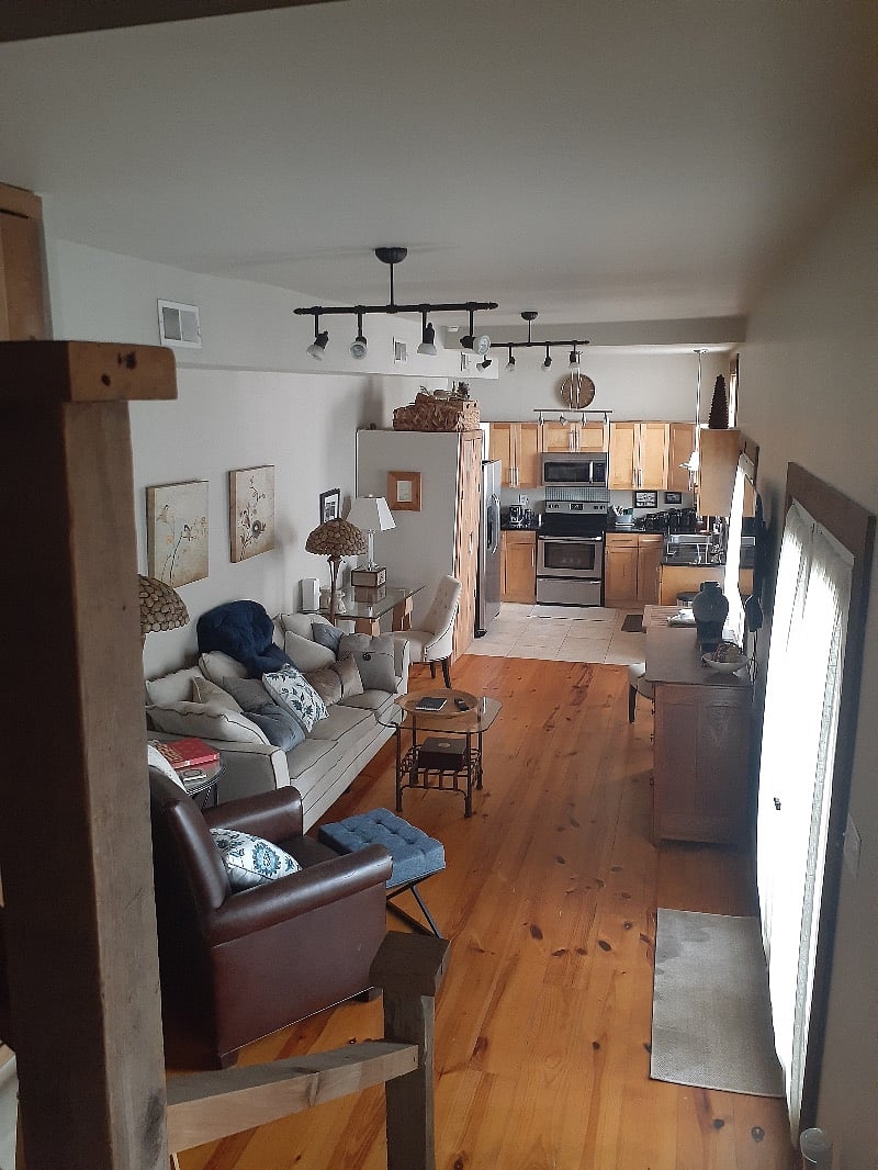 View from stairs into living, dining and cooking space downstairs. Windows look out onto and doors open out onto brick patio garden area and entry walkway.