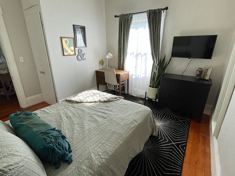 Bedroom with full bed, desk, smart TV and blackout curtains.
