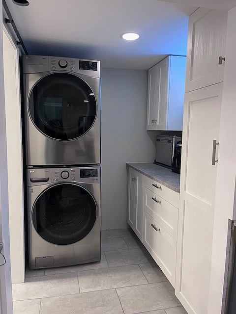 Full size front load stackable washer/dryer in laundry room with additional storage cabinets