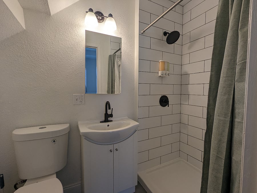 The bathroom has a shower that supplies hot and cold water; beside it is a toilet and a small sink!