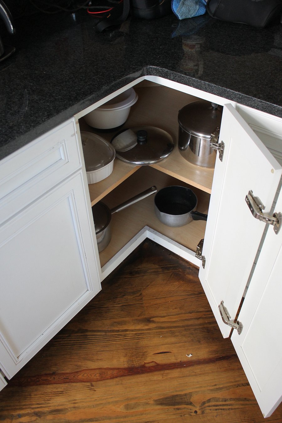 Open corner cabinet with pots, pans, and bowls. 