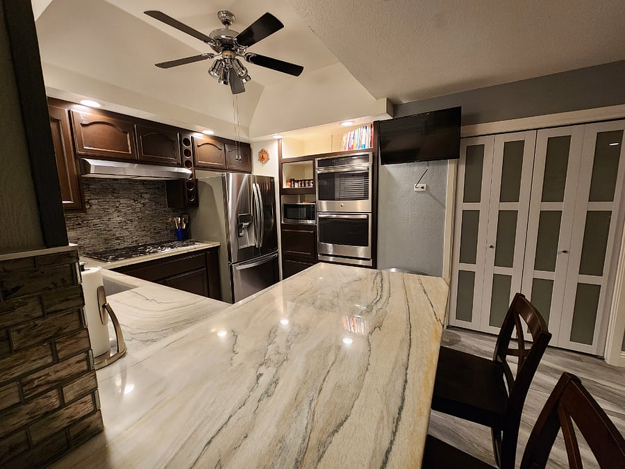 Kitchen has double ovens, TV, bar with chairs, microwave, and pantry.