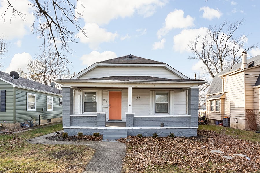 A charming single-story home with a welcoming front porch and a pop of color on the door.