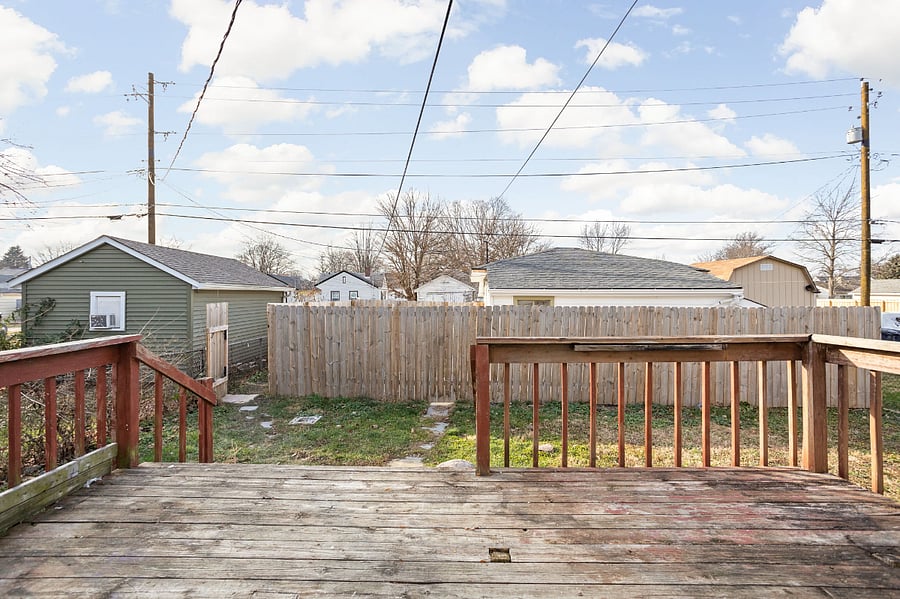 Backyard view from a wooden deck, featuring a fenced yard and neighboring houses in the background.