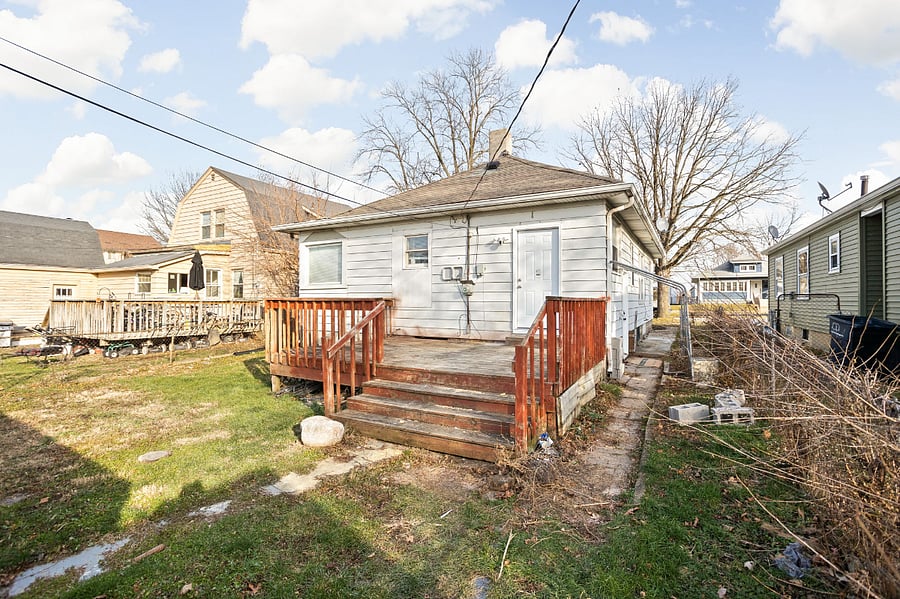 Backyard view of a home with a raised wooden deck and staircase, surrounded by neighboring houses.