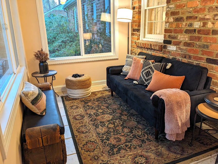 Sunroom Cozy seating area offers view of fenced woodland backyard and features remote-controlled sun shades.