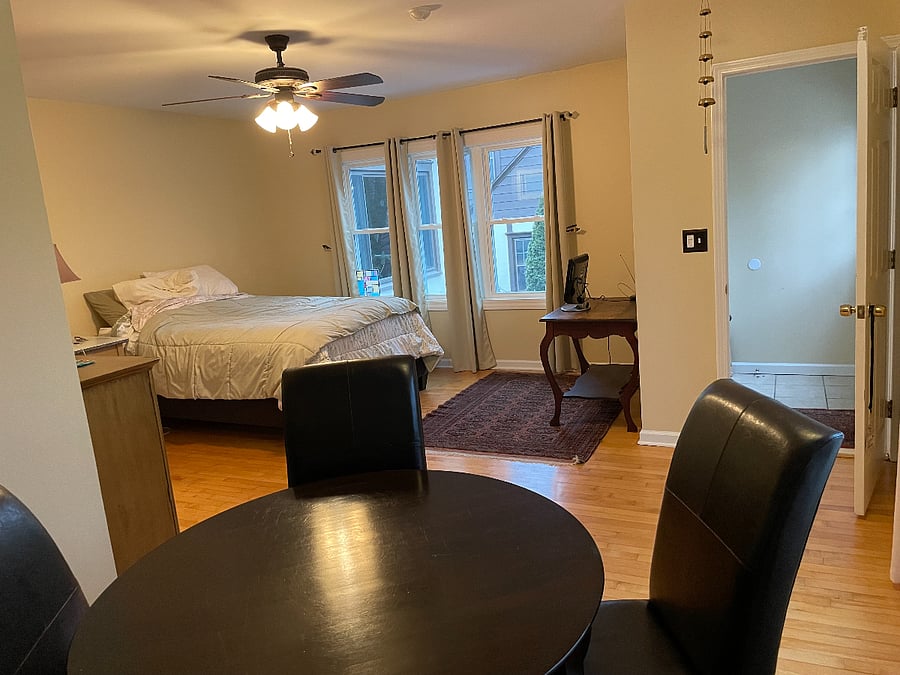 table w/4 chairs, queen bed, private entrance. Bathroom across from bed. 3 windows on the far side of the bed, 2 more to the right of the table.