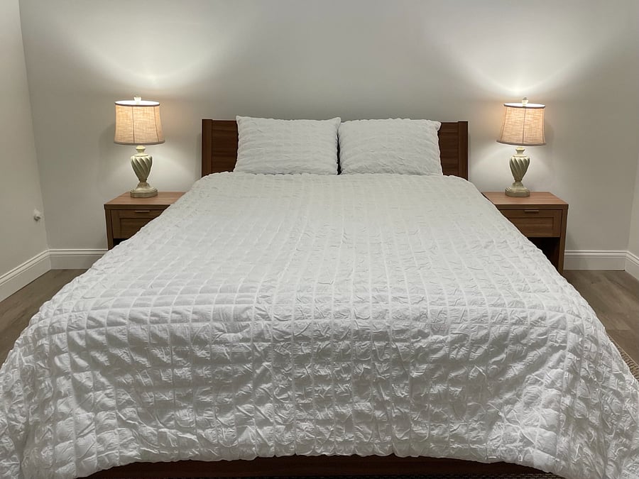 Bedroom with soft sheets and comforter, side tables and lamps.