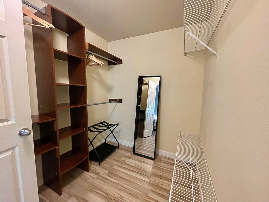 Large walk-in closet with ample shelving, luggage rack and full length free standing mirror.