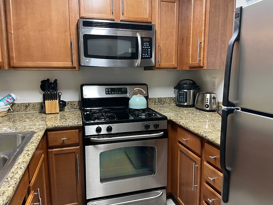 Full kitchen with stainless steel appliances, cooking utensils and dishware.