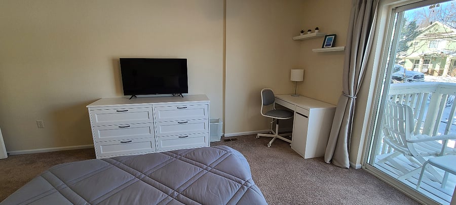 Master bedroom w/ desk workspace area, natural light from the balcony, and new Smart TV.