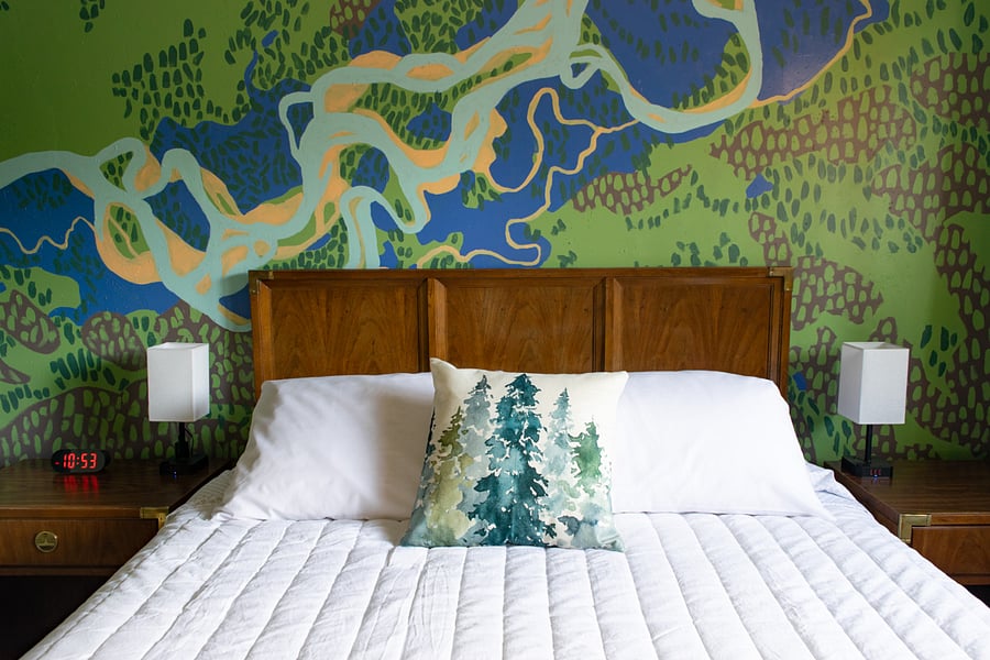 The Tanana Room with queen bed, ceiling and portable fans, extra pillows and blankets, and portable heater. The wall mural is a hand-painted overhead view of the Tanana Valley basin.