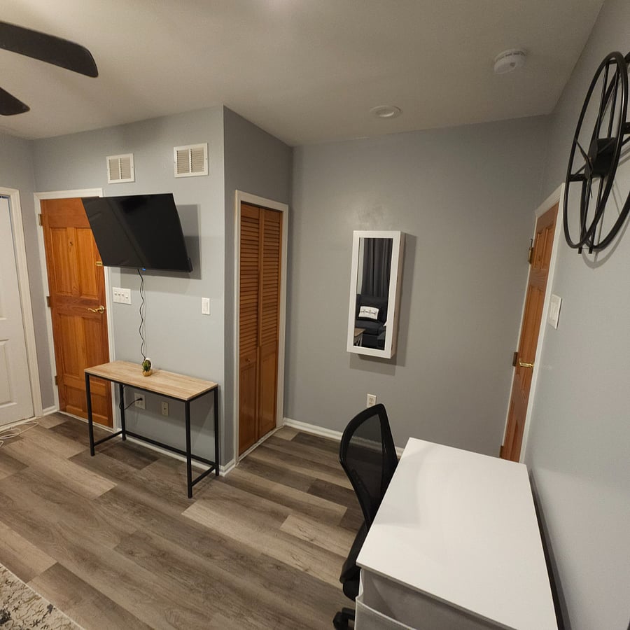 "Near Closet #2, the living room features a 40-inch extendable TV, Closet #1 for shoes and jackets, and a mirror doubling as an ironing board with storage, blending functionality and style."