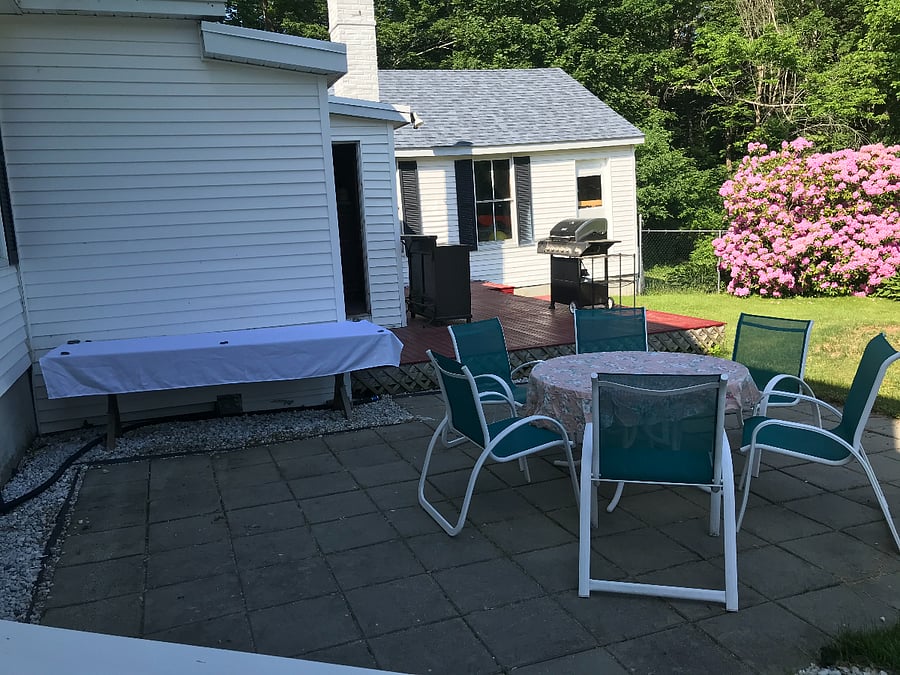 Large fenced in backyard with BBQ grill, firepit, table and chairs, and chaise lounges on the deck to relax.