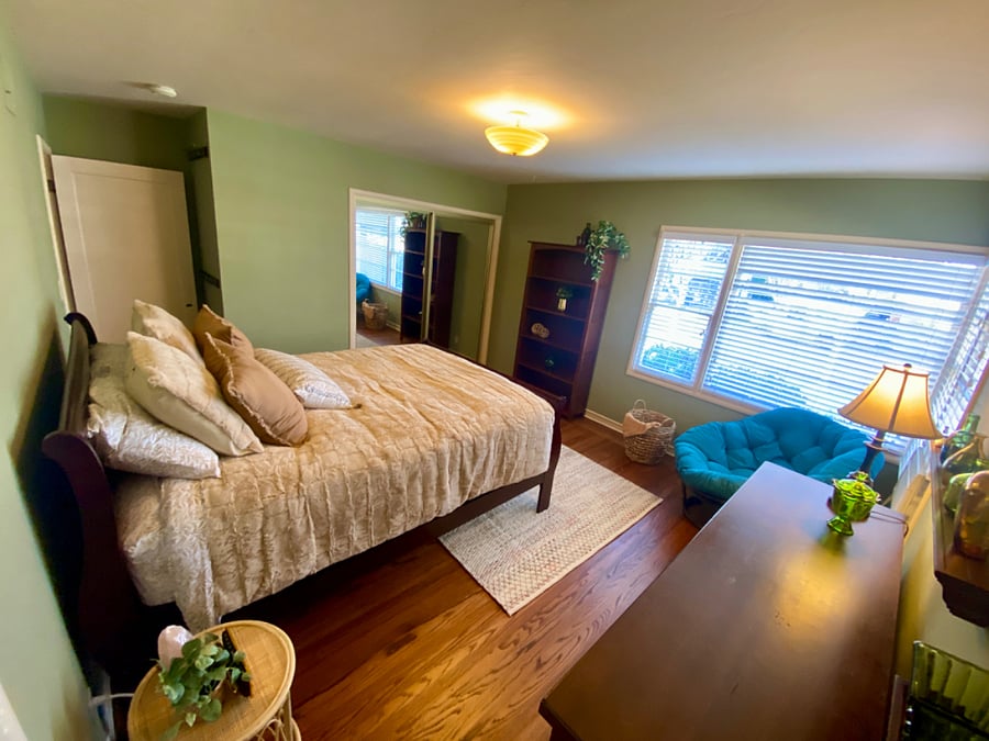Primary bedroom with Queen bed, rattan papasan chair, bookshelf and large closet with mirrored doors.