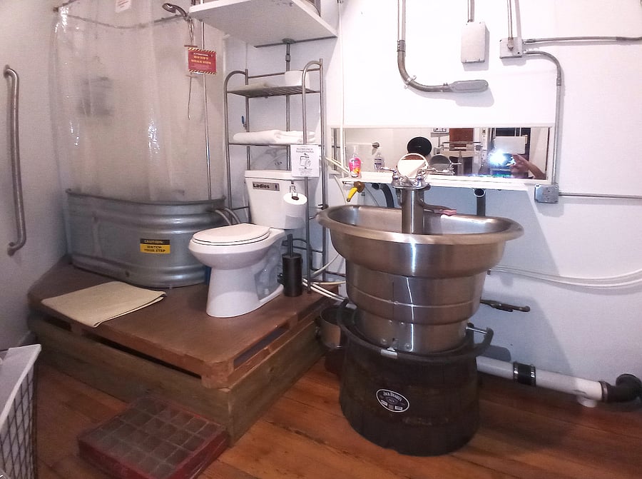Step into the distinctive bathroom, showcasing a trough turned into a tub, a sink crafted from a laboratory wash station atop a half barrel of Tennessee whiskey. Elevated plumbing platforms ensure easy access in case of maintenance needs.