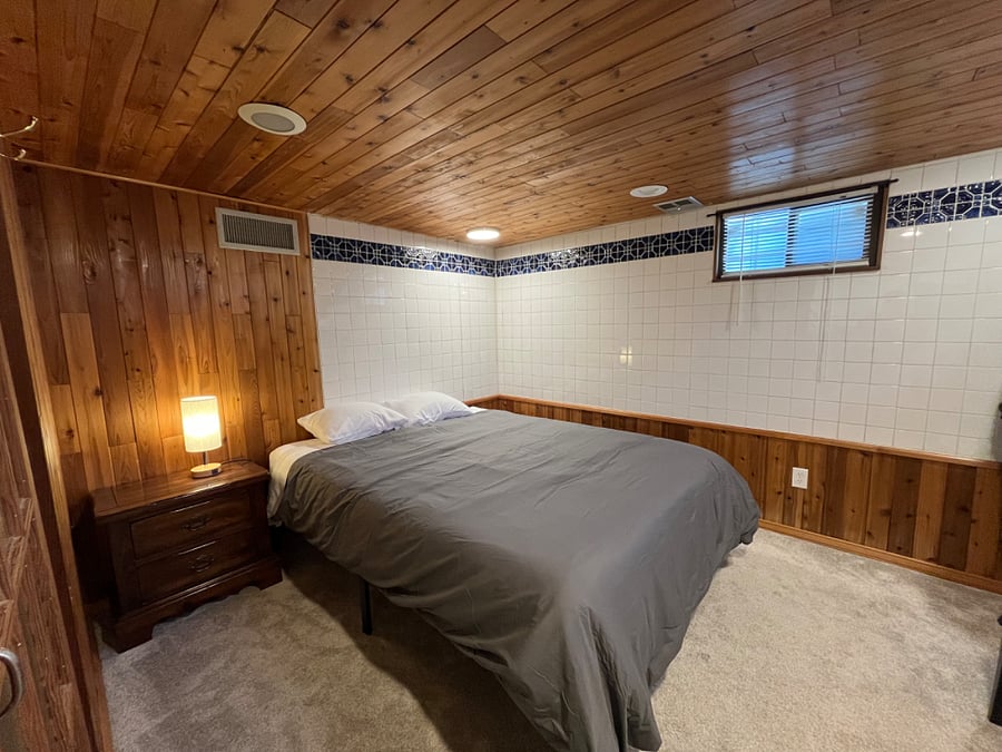 Bedroom with new queen-size memory foam bed, bedding, side table, lamp, and dresser. This room is partially tiled as it used to be a sauna!