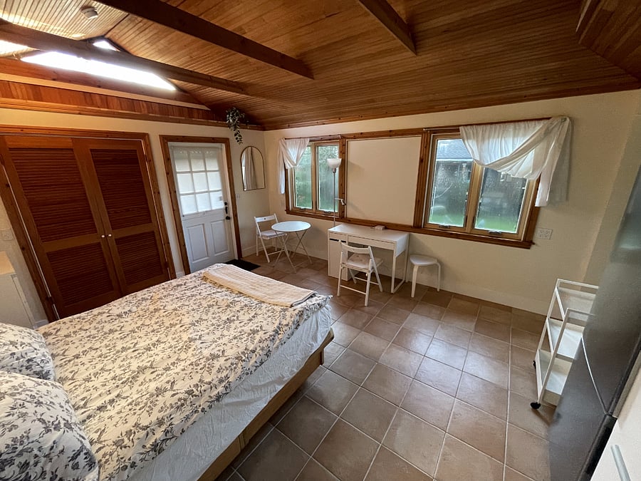 Main room facing entrance & front of cottage from bathroom door perspective. South-facing windows provide ample natural lighting, small table for dining, small desk available for laptop work or setting up TV your request, two comfortable folding chairs with padding available for dining or working.