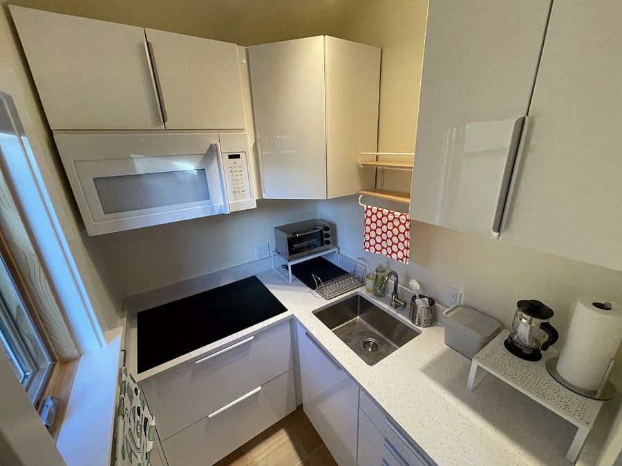 Kitchen perspective from kitchen doorway, 4-burner induction cooktop, hanging microwave, toaster oven, sink, and plenty of storage space for a kitchenette.
