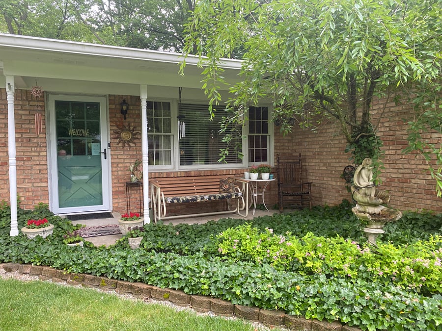 Front door entrance. Cozy covered front porch with beautiful annual flowers and bushes and plants with wonderful fragrances, a rocker and swinging bench with wind chimes.