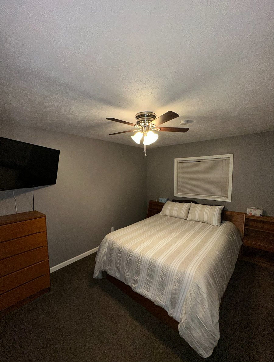 Upstairs master bedroom with oak bedframe that has built in drawers. Oak dresser, ceiling fan, and 43-inch mounted TV. 