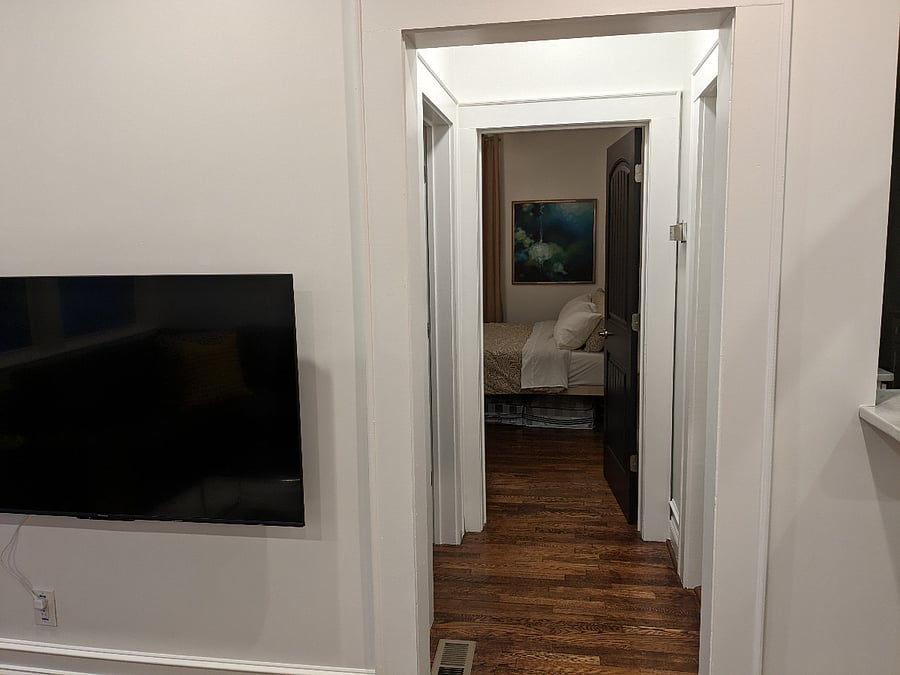 Short hallway connecting living room to primary bathroom (left) primary bedroom (ahead) and kitchen (right).