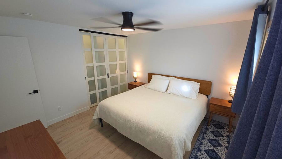 Main bedroom with Sleep Number king bed, 6-drawer dresser, two nightstands with storage, lamps with USB ports, air purifier, blackout curtains, mirror, and walk-in closet with hangers, dirty laundry hamper, and shelves. Extra blankets and two sets of sheets in storage bins under bed.
