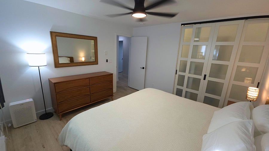 Main bedroom with Sleep Number king bed, 6-drawer dresser, two nightstands with storage, lamps with USB ports, air purifier, blackout curtains, mirror, and walk-in closet with hangers, dirty laundry hamper, and shelves.
