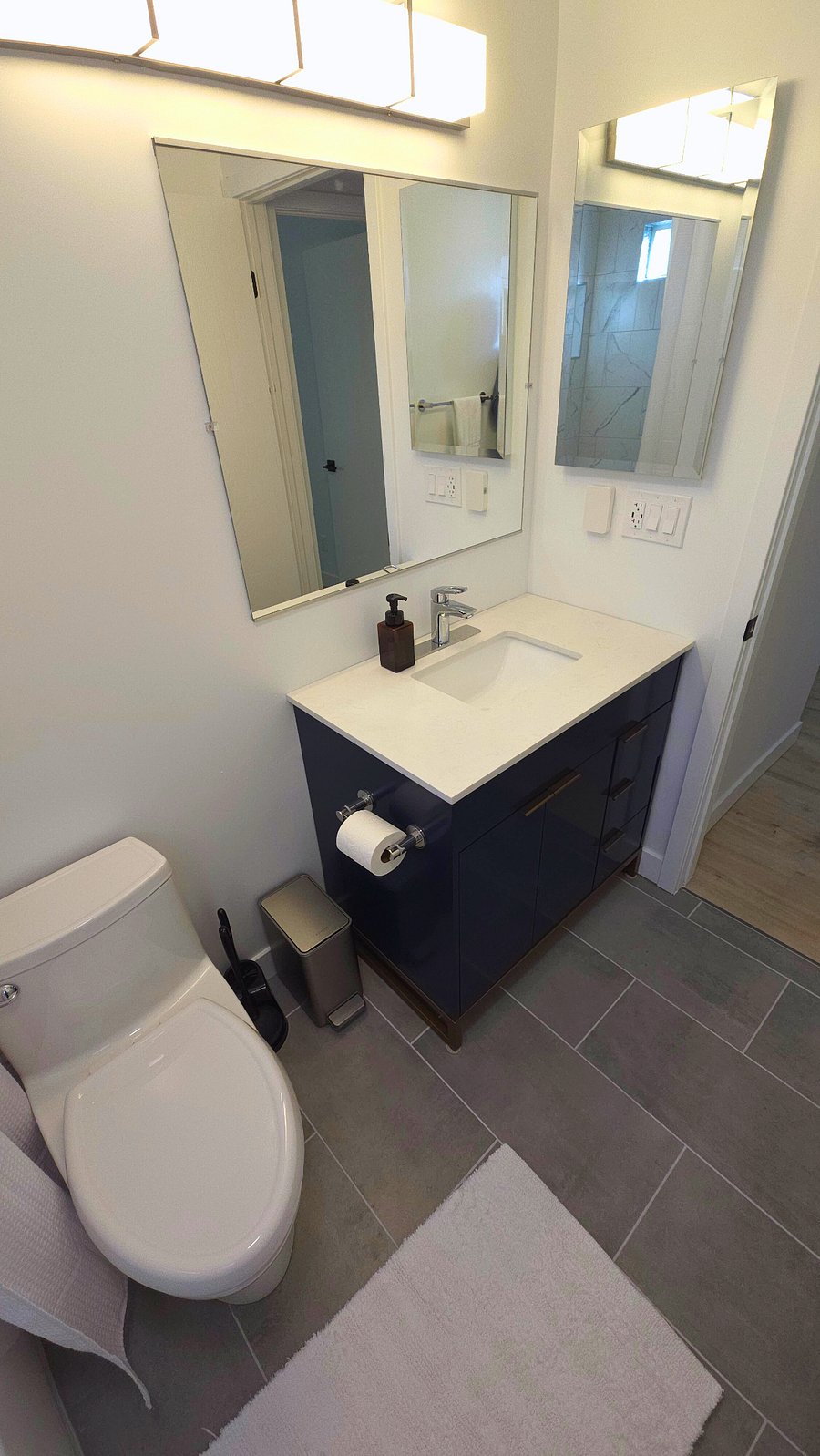 One piece American Standard seat height toilet with elongated bowl. Stainless steel trash can, toilet brush and plunger. Dimmable vanity light. Separate bathroom exhaust fan with light.