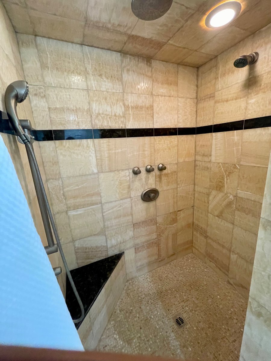 Beautiful honey onyx shower with a granite accent, bench in shower, and 2 shower heads.