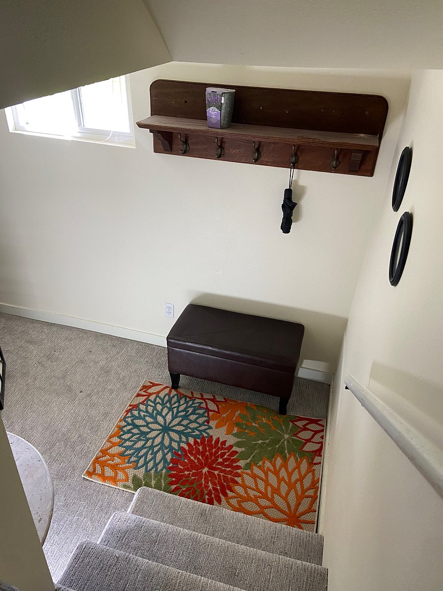 Looking down the stairs into the entryway with storage bench, hooks, shelf and table