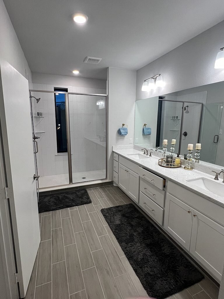 Spacious walk-in shower connected to the primary suite with dual sink vanity and large mirror.