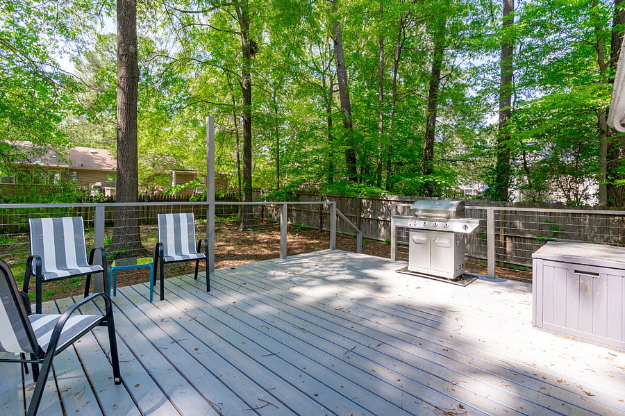 Large back deck complete with outdoor furniture, propane grill, and a view of the fenced in backyard.
