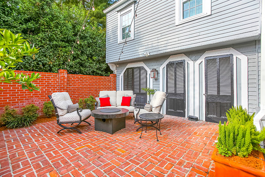 Private brick courtyard with Bevelo cooper gas lanterns, wrought iron seating, and plush Dream cushions. A lovely outdoor space for relaxing with a fire pit and grill