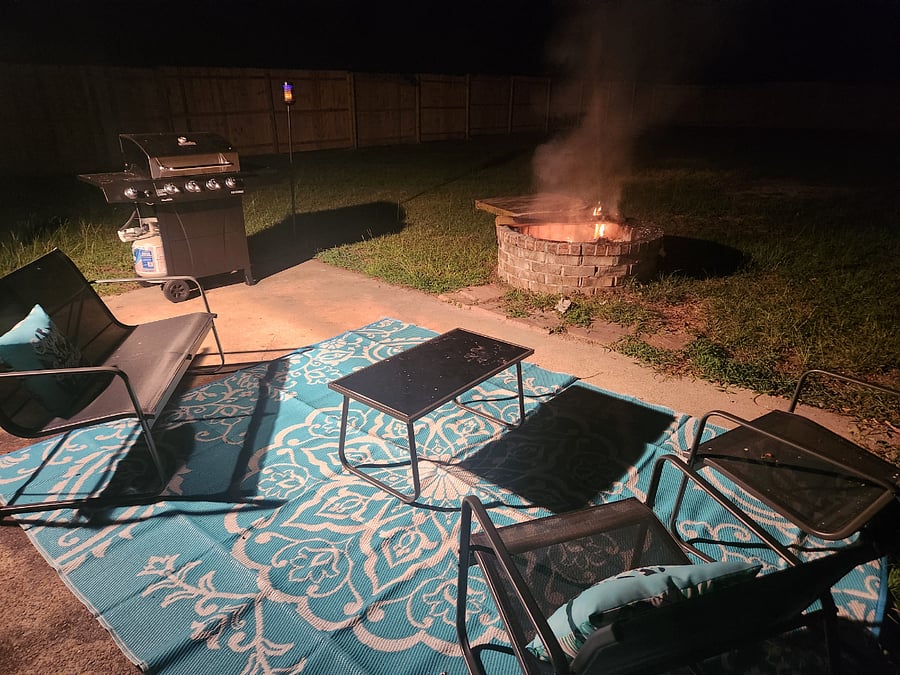 Outdoor area in back yard has a large fenced yard with a fire pit, seating for 4 and a grill with all needed grill tools.