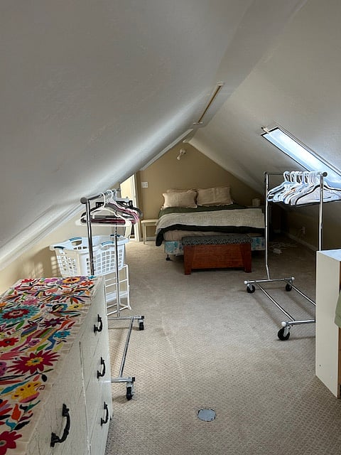Looking toward queen bed from the rest of the bedroom; with hanger racks and dresser.