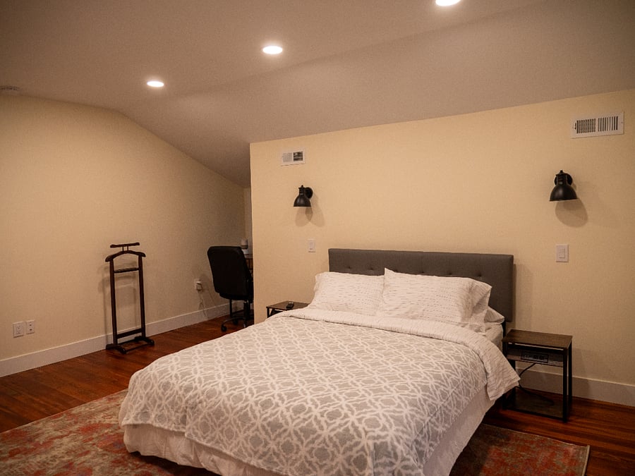 Room #3. Queen bed, work station, Smart TV, bureau, & closet. Features an en suite bathroom, extra floor space, bedside lighting, & a rocking chair