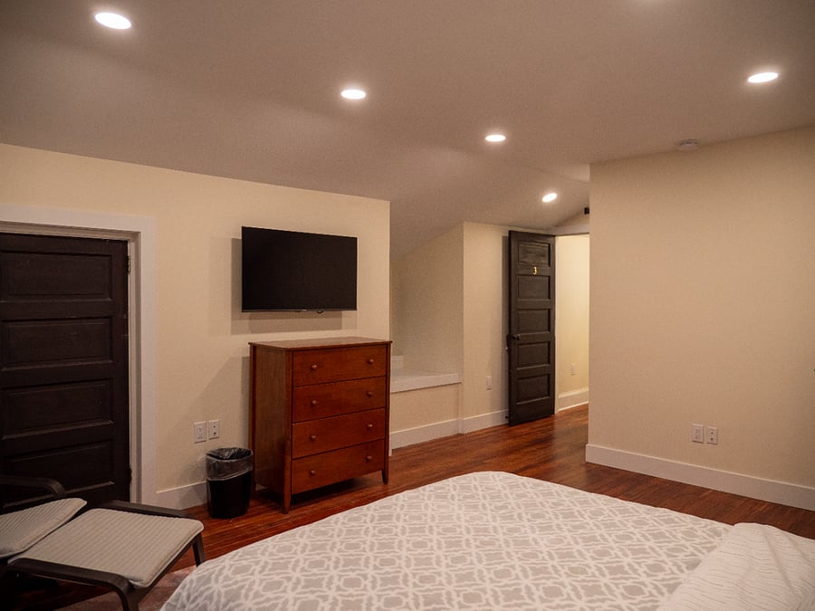 Room #3. Queen bed, work station, Smart TV, bureau, & closet. Features an en suite bathroom, extra floor space, bedside lighting, & a rocking chair