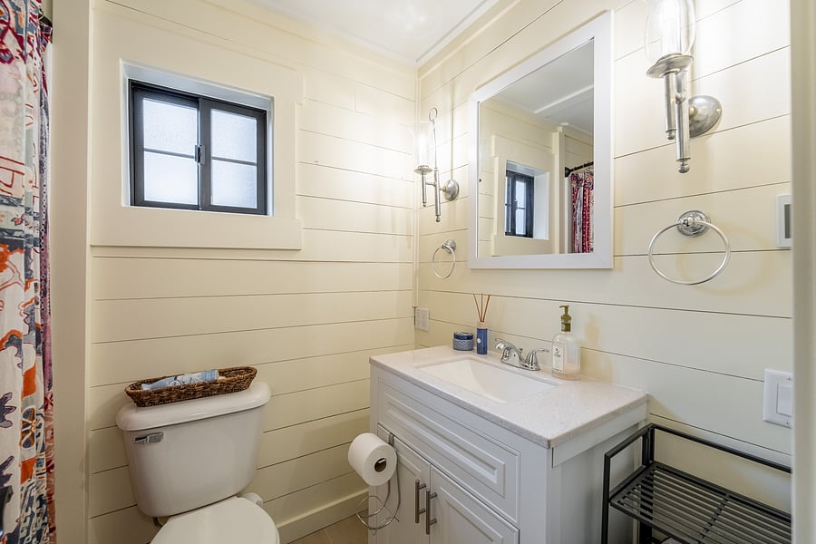 Compact full bathroom with heated tile floors, frosted windows, ventilation and surprisingly generous storage.