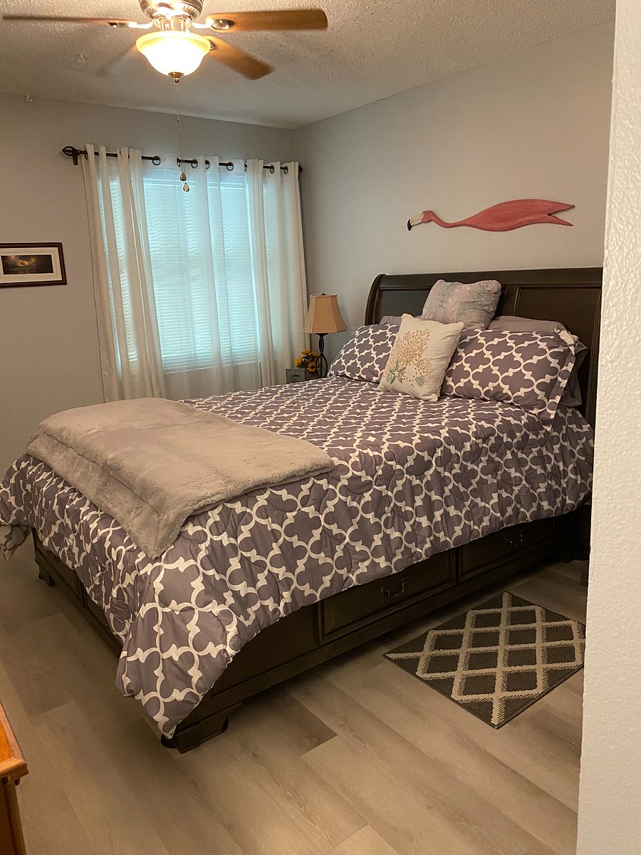 Queen size bed in master bedroom with two nightstands, only one visible, on far side of bed with lamp.