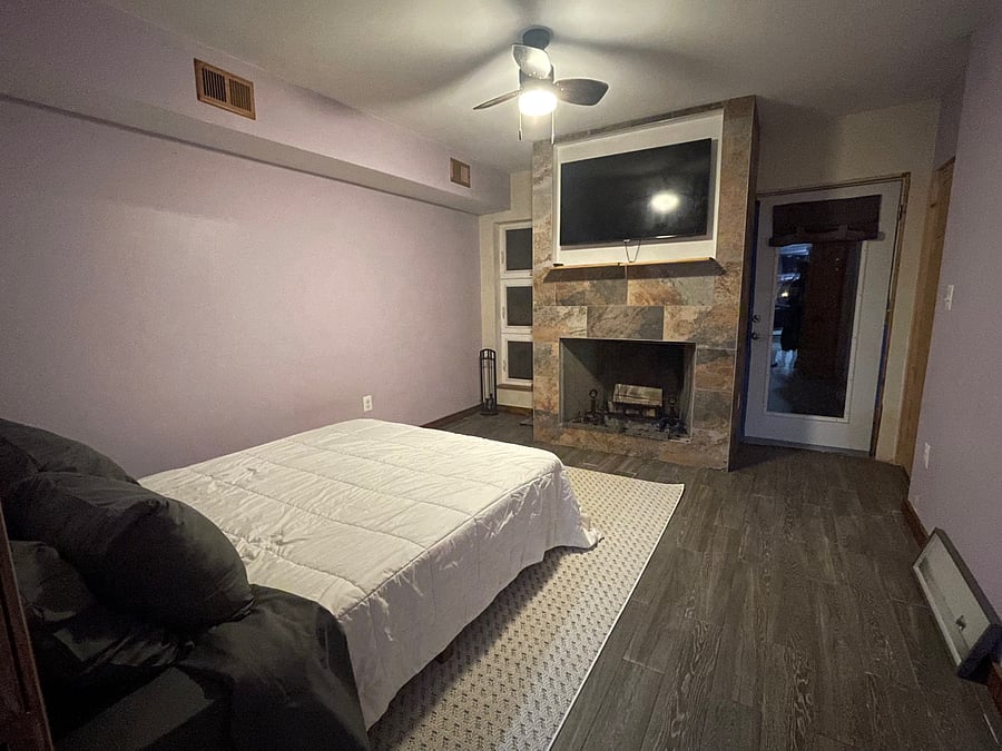 Bedroom retreat features a queen bed, wall-mounted smart TV, fireplace and private balcony with oversized wicker egg chair.