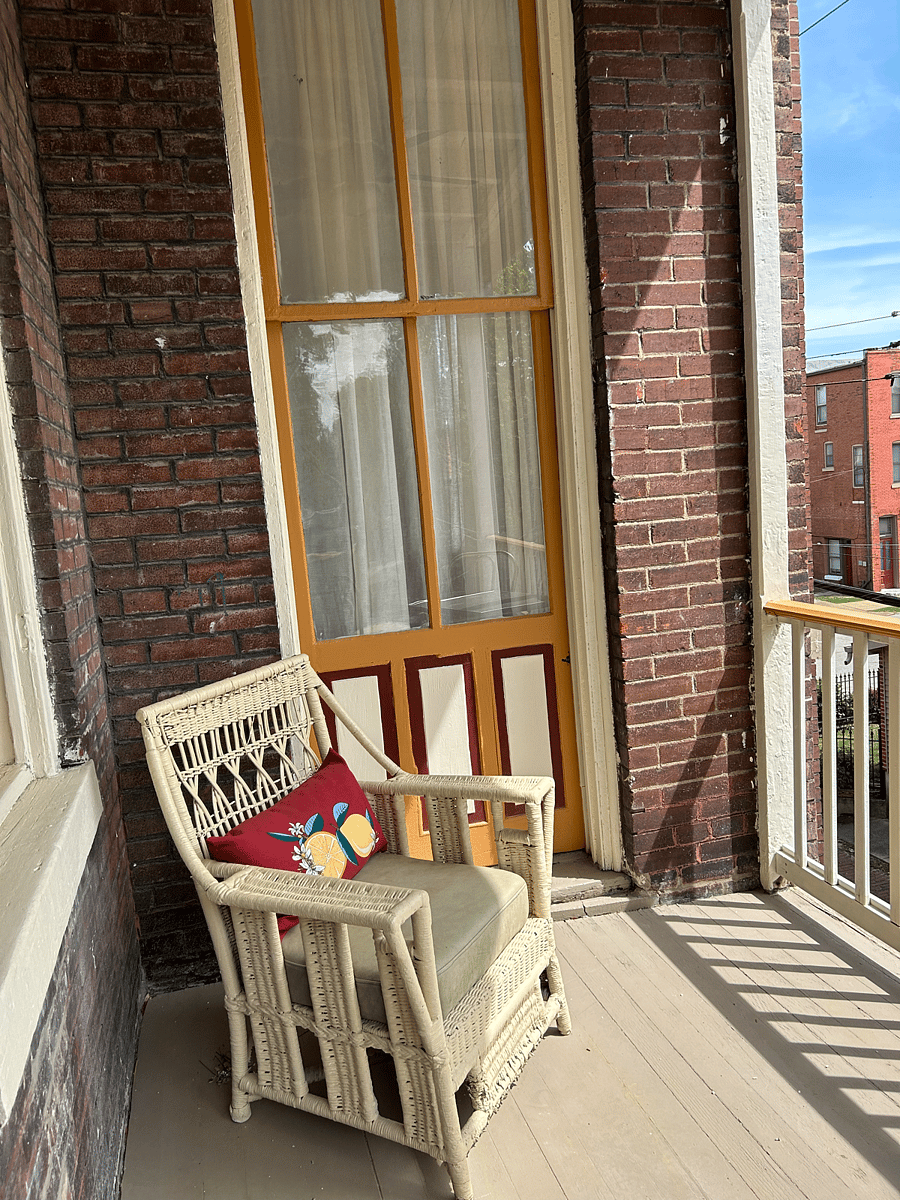 Side porch off kitchen with comfy chair and table. Outdoor space looking out over this sweet neighborhood!