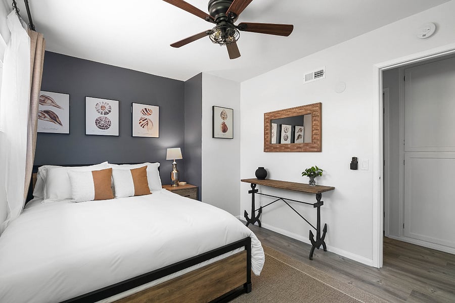 Bed includes "Below Zero" brand cooling down comforter and hotel brand pillows. Door on right leads to hallway showing hallway linen closet.