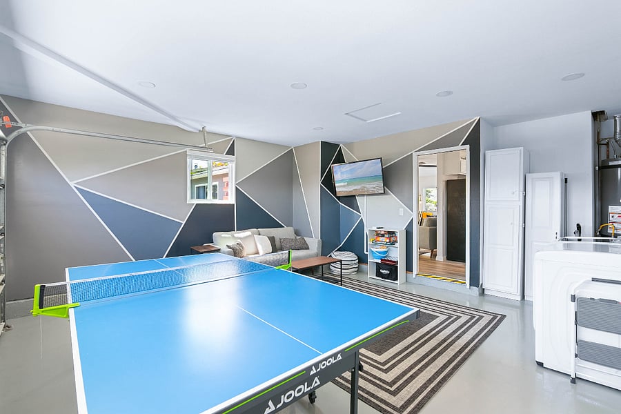 View from garage door showcasing ping pong table, laundry area, and game room seating area. Door shows entrance to kitchen and reading area. Cabinet not available for guest use.