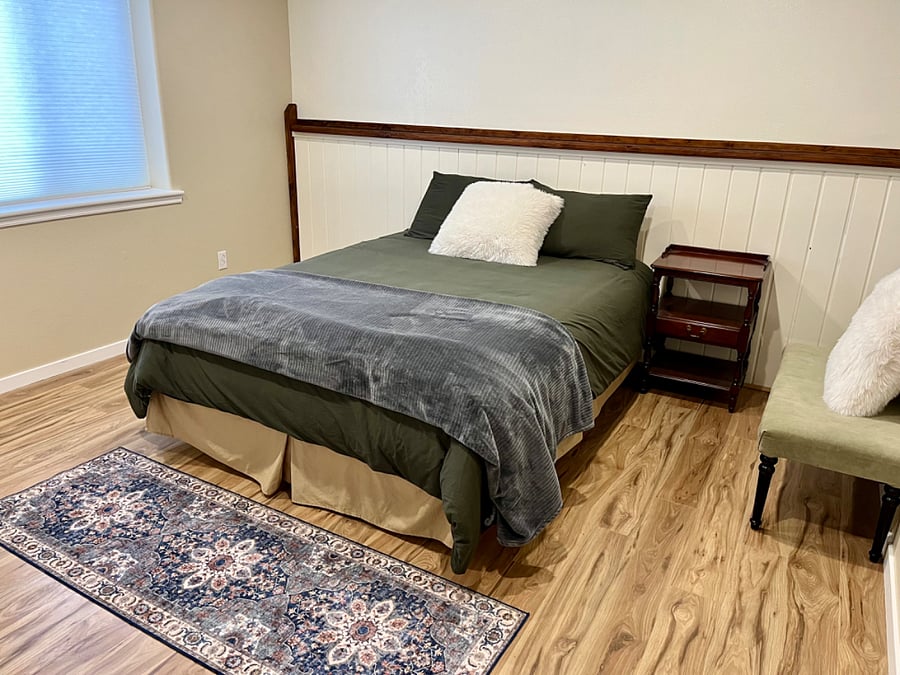 1st room - queen sized bed, bedside table, & footstool.