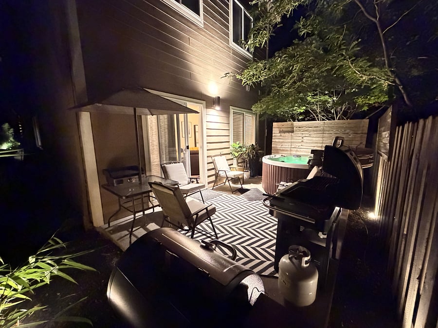 Back patio in the evening featuring mood lighting, a hot tub, an electric smoker barbecue, and a standard propane grill.